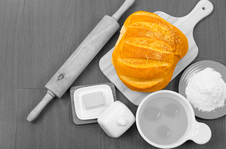 Beautifully colored loaf of bread stands out as eggs, cheese, roling pin and flour are in black white .の写真素材