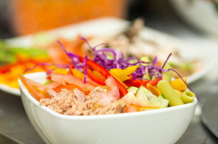 Closeup delicate fresh presentation of tuna salad in white bowl with colourful vegetables such as cole robbie, capsicum, cucumber and tomatoes.の写真素材