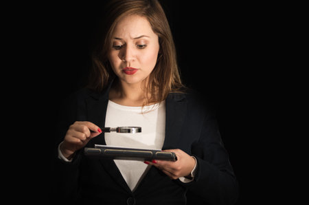 Young woman holding magnifying glass in front of face, slightly tilting head forward looking through...