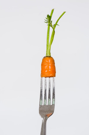 Closeup silver fork with small piece of organic carrot including stem and white background.の写真素材