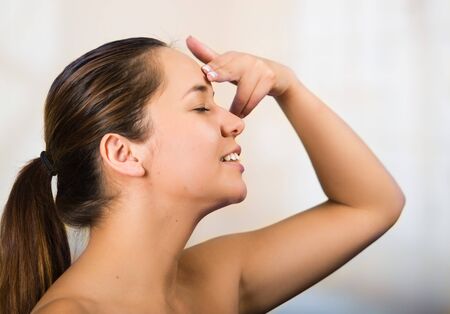 Pretty young healthy hispanic woman headshot with naked shoulders, applying cream to face using hands.の写真素材