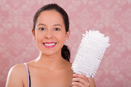 Brunette woman holding white fluffy cleaning brush while smiling to camera, pink background.の写真素材