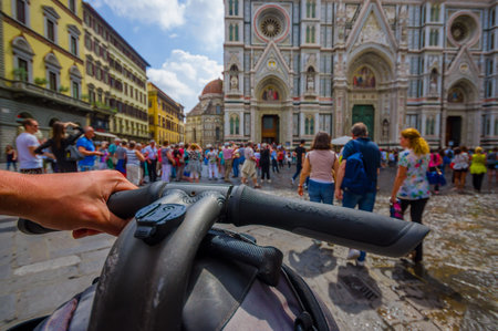 FLORENCE, ITALY - JUNE 12, 2015: Bycicle handlebars with one hand ridding close up, stone street and a nice view of the cathedral in front. People crossingのeditorial素材