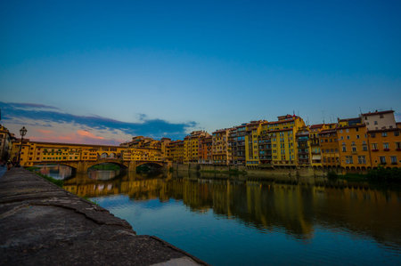 FLORENCE, ITALY - JUNE 12, 2015: FLORENCE, ITALY - JUNE 12, 2015: Sunset foto over Arno river, Old Bridge and Vasari corridor at the end with great sky colors. Old houses on the side.のeditorial素材