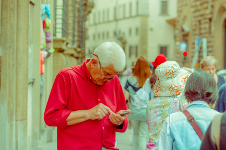 FLORENCE, ITALY - JUNE 12, 2015: Unidentified old man looking with enough concentration to his mobile phone, red shirtのeditorial素材