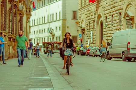 FLORENCE, ITALY - JUNE 12, 2015: Woman ridding a nice bycicle with a shopping bag, walkers on the side and a bus comming. Summerのeditorial素材