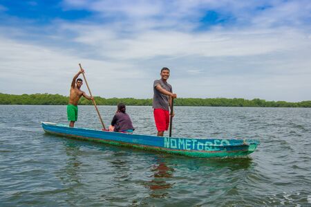 Muisne, Ecuador - March 16, 2016: Two people standing inside green canoe while one more person sitting down, out on pacific ocean, beautiful forest coastline background.のeditorial素材
