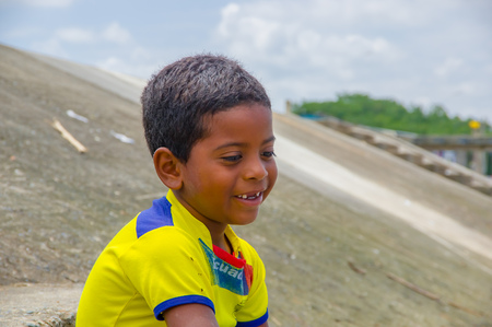 Muisne, Ecuador - March 16, 2016: Kid sitting outdoors with yellow football shirt on and smiling.のeditorial素材