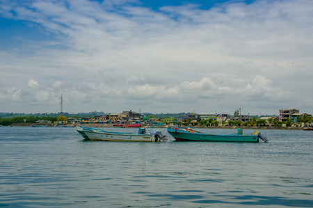 Muisne, Ecuador - March 16, 2016: Traditional fishing boats tied together at sea, city in background and beautiful blue sky.のeditorial素材