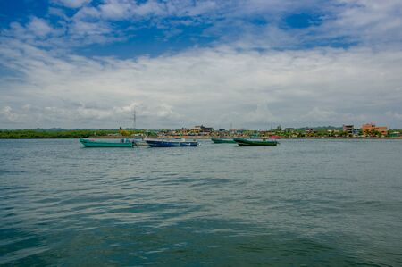 Muisne, Ecuador - March 16, 2016: Traditional fishing boats tied together at sea, city in background and beautiful blue sky.のeditorial素材