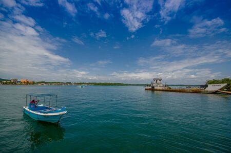 Muisne, Ecuador - March 16, 2016: Small rusty ferry connecting island to mainland parked by local pier, awaiting passengers, beautiful blue sky.のeditorial素材