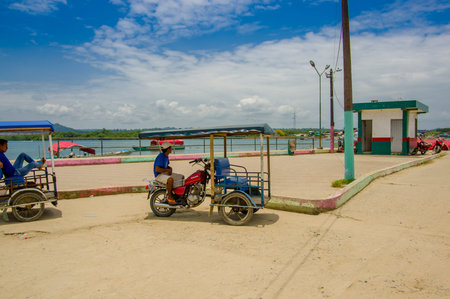 Muisne, Ecuador - March 16, 2016: Local tuktuk driver sitting in his vehicle next to ocean waiting...