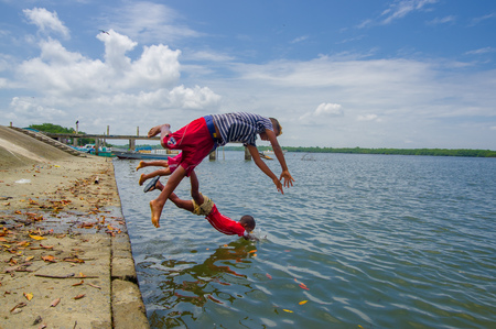 Muisne, Ecuador - March 16, 2016: Kids diving and swimming in pacific ocean from stone surface with clothes on.のeditorial素材
