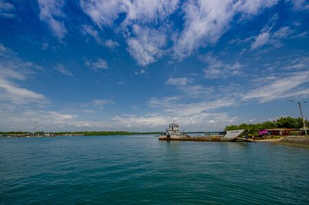 Muisne, Ecuador - March 16, 2016: Small rusty ferry connecting island to mainland parked by local pier, awaiting passengers, beautiful blue sky.のeditorial素材