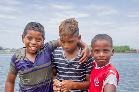 Muisne, Ecuador - March 16, 2016: Adorable local kids posing happily for camera embracing each other with pacific ocean in background.のeditorial素材