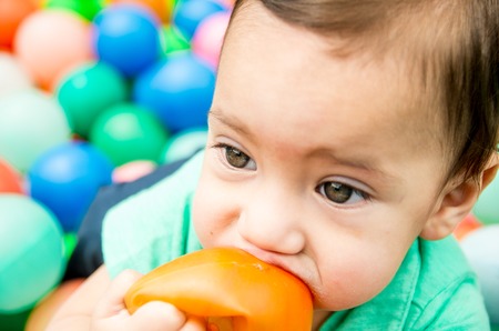 Cute baby boy wearing turquoise t-shirt and combed hair, sitting outside on grassy surface playing around.の写真素材