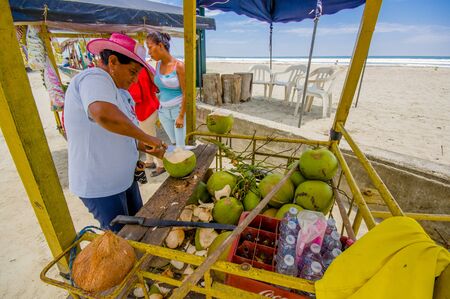 Muisne, Ecuador - March 16, 2016: Local street vendor working and using knife on green coconuts, beachside pacific ocean.のeditorial素材