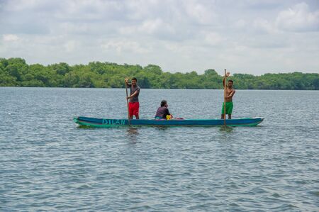Muisne, Ecuador - March 16, 2016: Two people standing inside green canoe while one more person sitting down, out on pacific ocean, beautiful forest coastline background.のeditorial素材