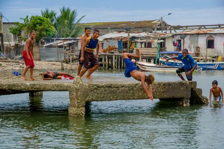 Muisne, Ecuador - March 16, 2016: Local kids and teenagers playing happily jumping from pier into ocean, posing for camera laughing, beautiful blue sky.のeditorial素材