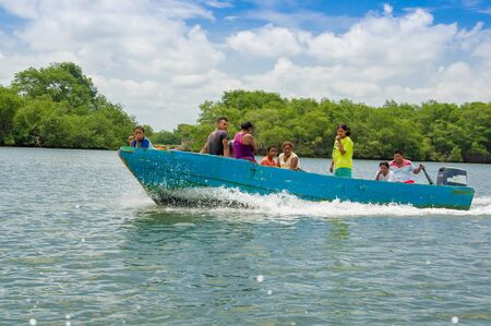 Muisne, Ecuador - March 16, 2016: Group of people, adults and kids inside typical blue fishingboat driving alongside shore, green trees background.のeditorial素材