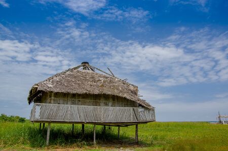 Muisne, Ecuador - March 16, 2016: Old traditional bungalow sitting on woden poles above grassy surface, beautiful blue sky.のeditorial素材