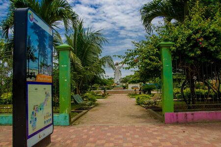 Muisne, Ecuador - March 16, 2016: Entrance to local park with statue of Jesus inside, green trees and red stone surface.のeditorial素材