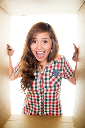 Screaming girl inside a cardboard box, two hands holding the borders in a white background.の写真素材