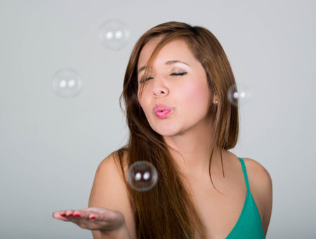 Woman blowing some soap bubbles, closed eyes and extended hand, gray background.の写真素材