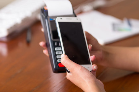 Two woman hands holding a credit card machine and mobile phone, a reader can scan a code to pay the...