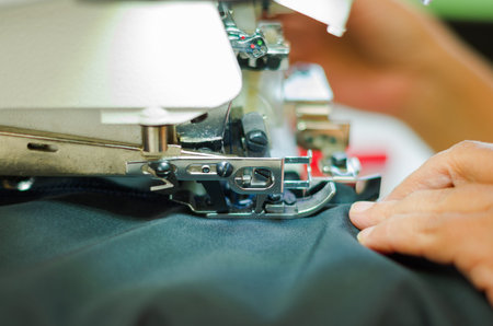 Close up of woman hands holding a black fabric and sewing machine with needles.の写真素材