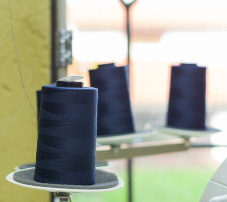 Blue spool of thread ready to be used in a sewing machine, behind other spools.