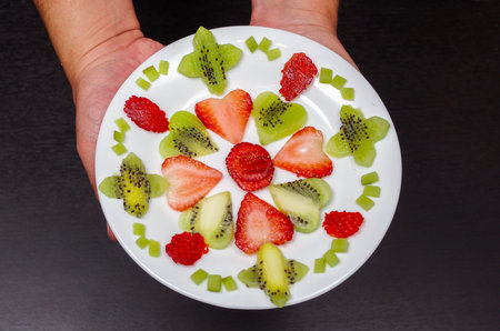 Sliced kiwi and strawberries lying in neatly placed pattern on white plate, as senn from above.