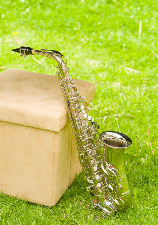 Beautiful golden saxophone standing up against chair on grassy surface.の写真素材