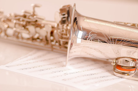 Closeup partly view of shiny saxophone lying on musical notes paper.