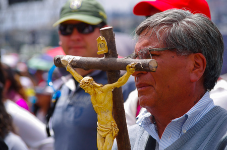 QUITO, ECUADOR - JULY 7, 2015: Old man holding a big cross with jesus body representation, pope Francisco mass with lots of people.のeditorial素材