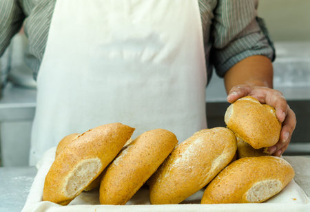 Pile of fresh bread loafs, baker standing behind with only apren and arms visible, bakery concept.