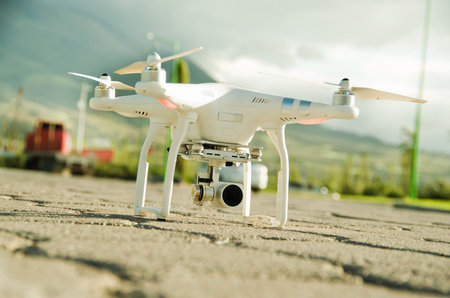 White drone with camera mounted underneath sitting on concrete surface, mountain landscape...