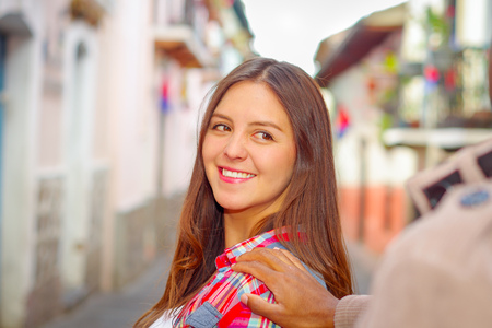 Pretty brunette woman turns around smiling while boyrfriends hand touches her shoulder, vibrant colors and blurry urban background.の写真素材