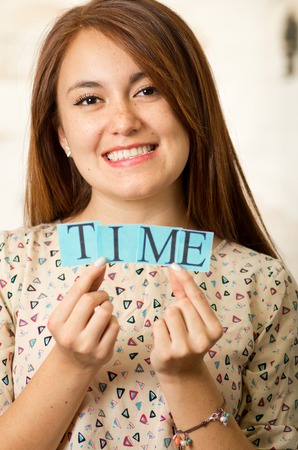 Headshot charming brunette woman holding up small letters spelling the word time and smiling to camera.の写真素材