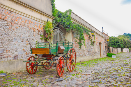 COLONIA DEL SACRAMENTO, URUGUAY - MAY 04, 2016: old green cart with red tires parked outside an ancient house.のeditorial素材