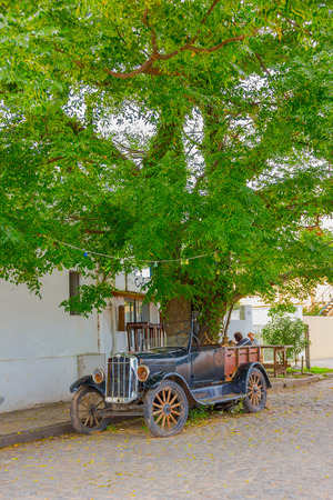 COLONIA DEL SACRAMENTO, URUGUAY - MAY 04, 2016: ancient classic car parked under a tree next to the sidewalk.のeditorial素材