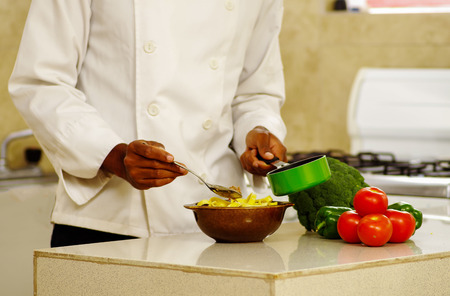 Happy chef wearing white clothes preparing bowl of food in professional kitchen, smiling while finishing last touch.の写真素材