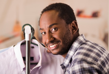 Handsome young man standing inside wardrobe going through rack of different shirts hanging, fashion concept.の写真素材