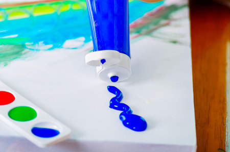Closeup white sheet with colors on it, squeezing blue tube paint onto surface.