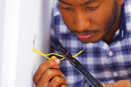 Man wearing white and blue shirt working on electrical wall socket wires using screwdriver, electrician concept.の写真素材