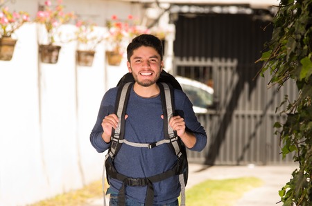 Young happy man wearing casual clothes and backpack posing for camera, smiling, garden environment, backpacker concept.の写真素材
