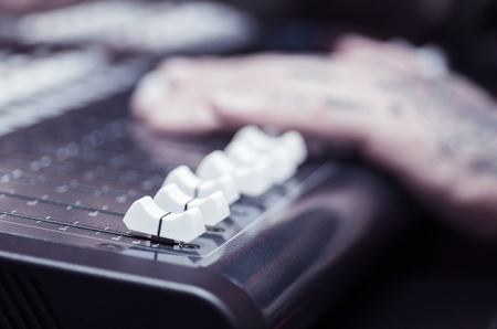 Closeup of hands covered with tattoos working on mixer console, pushing faders, studio equipment concept.の写真素材
