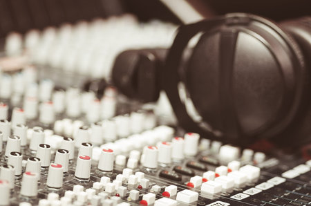 Closeup mixing console with headphones on top, faders and knobs background, artistic studio...