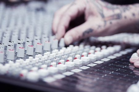 Closeup of hands covered with tattoos working on mixer console, twisting knobs, studio equipment concept.の写真素材