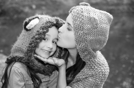 Mother with daughter both wearing hoodies and warm clothing sitting outdoors embracing happily, green nature background, black white edition.の写真素材
